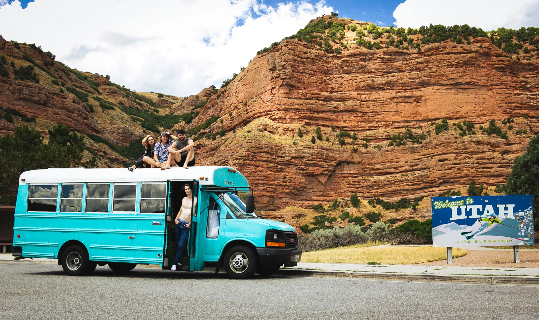 The cast and crew of Childish Things (Guinevere Berthelot, Tyler Sebago, Nick Cassidy, and Cash Cassidy) pose for a photo aboard their blue short bus at a rest stop in Utah.